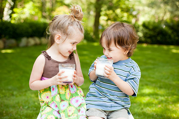 Color image of a little boy and a little girl sitting outside drinking a glass of milk and smiling at each other. Focus is on little boy.