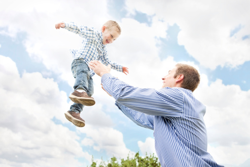 A stock photo of a young father and his happy son playing together outdoors.