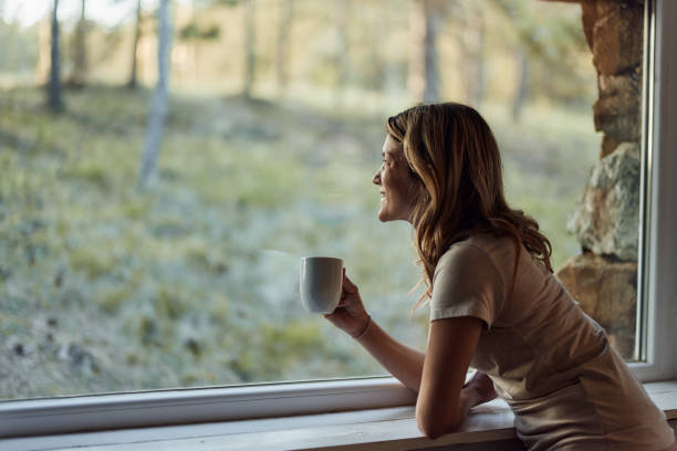 istock Happy woman looking through window during coffee time at home. 1677640024
