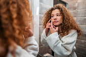 Young Woman Popping A Pimple In The Bathroom Mirror