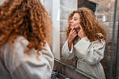 Young Woman Popping A Pimple In The Bathroom Mirror