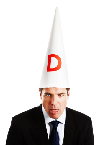 Humorous study of a businessman in formal suit wearing a dunce's cap, open mouthed, rolling his eyes and looking really dumb! Probably made a really stupid mistake! Isolated on white.