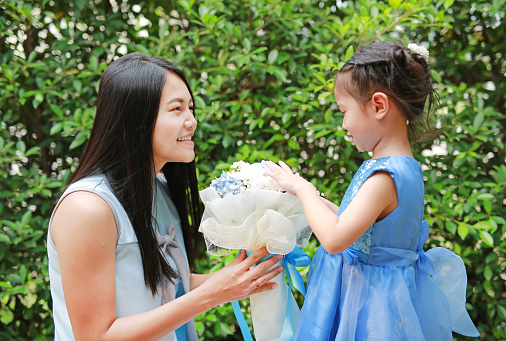 Asian child girl giving bouquet of flowers for her mother in the garden.