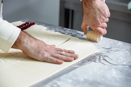 Patissier using small rolling cutter to make openings on upper dough sheet on the small business kitchen counter