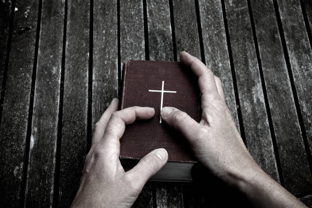 Mature person's hands holding old bible, wood background