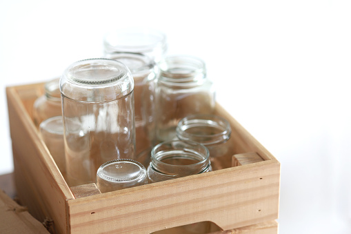 A wooden box is filled with empty glass jars against white background, all prepared for recycling. This setup showcases a sustainable lifestyle and responsible waste management.