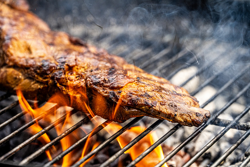 Process of preparing two pork or beef steaks. Meat roasted on metal portable summer barbecue BBQ grill with bright flaming fire, smoke and ember charcoal. Cooking and restaurant concept. Close up