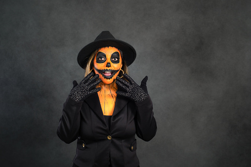Woman made up as a pumpkin to celebrate Halloween making surprise gesture. Dark background with copy space.