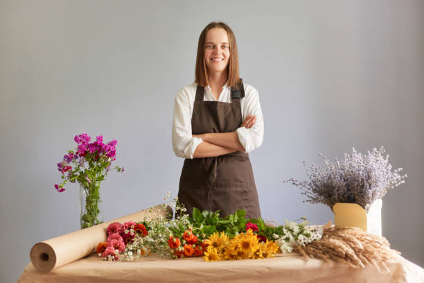 istock Creative floral workspace. Small business floristry. Assorted floral collection. Blossom-themed decor. Confident woman florist in flower shop standing isolated over gray background 1677776427