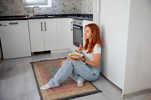 nutritionist girl eats healthy food at home in the kitchen sitting on the floor by the fridge