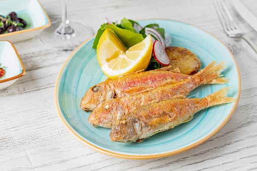 Delicious grilled red mullet fish with garnishes like lemon, greens and onions