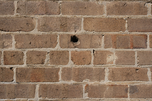 A small hole in a brown brick wall.