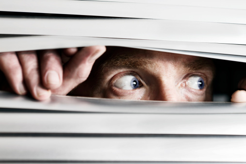 This terrified man looking out to the side  through a venetian blind could be witnessing a crime, watching the suspicious behavior of neighbors, or simply a paranoid, isolated shut-in.  
