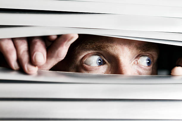 Fearful man looking sideways through venetian blind This terrified man looking out to the side  through a venetian blind could be witnessing a crime, watching the suspicious behavior of neighbors, or simply a paranoid, isolated shut-in.   peeking stock pictures, royalty-free photos & images
