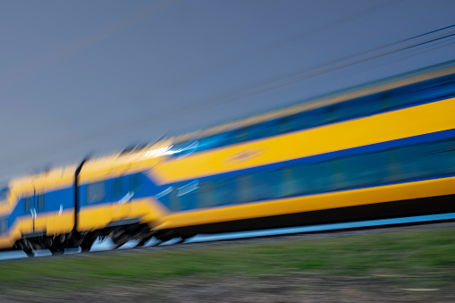 Intercity train of the Dutch Railways driving through the countryside landscape on the Hanzelijn in The Netherlands during springtime. The train is blurred caused by the speed its traveling.