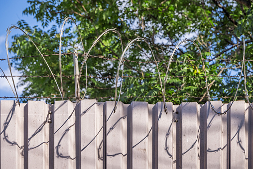 Barbed wire casting shadows on a metal fence, which is a typical sight in Queens which is a suburb to New York city