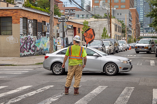 27th Street, Long Island City, Queens, New York, USA - August 23th 2023:  Hard hat worker with slow sign in the middle of the street in connection with a construction work