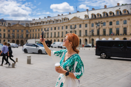 Beautiful mature woman using modern technology in her visit to Paris, taking a selfie with her smart phone for sharing on social media