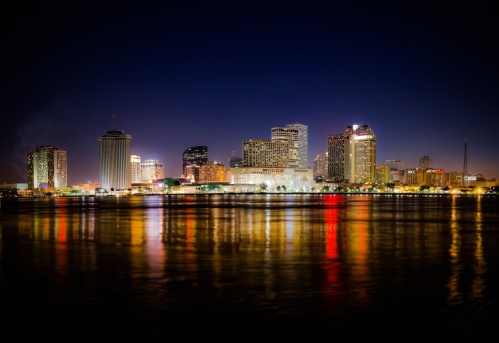 City of New Orleans by Night, with the skyscrapers illuminated, reflected in the water of the Mississippi river.