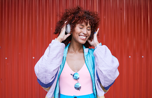 Music, dance and headphones with a retro woman on a red background in the city for energy or freedom. Radio, smile and streaming audio with a happy young afro person listening to sound for wellness