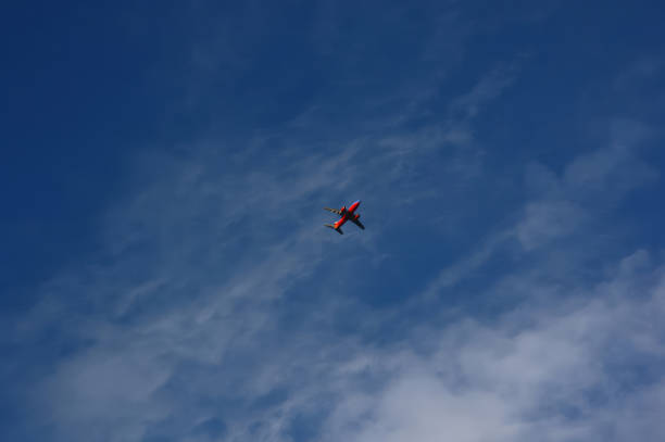 istock A blue and red plane flying in a blue sky with wispy clouds. 1677892824