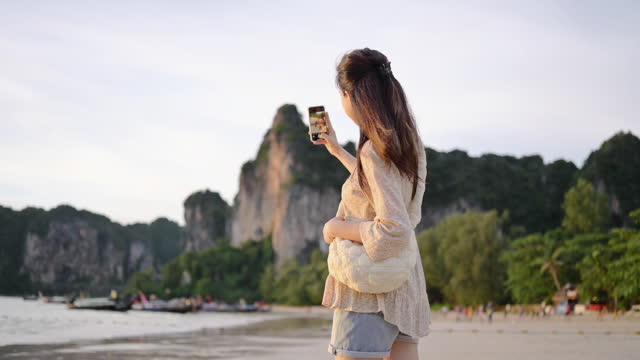 Solo trip Generation z asian using mobile 6G social media sharing sunset sky Railay beach sea in krabi south thailand asia