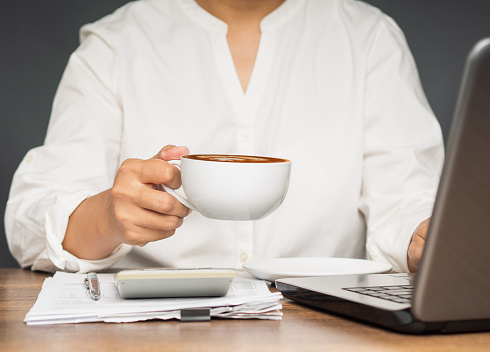 Businesswoman hand holding a cup of coffee sitting working at the office. Close-up photo. Beverage and relaxation concept