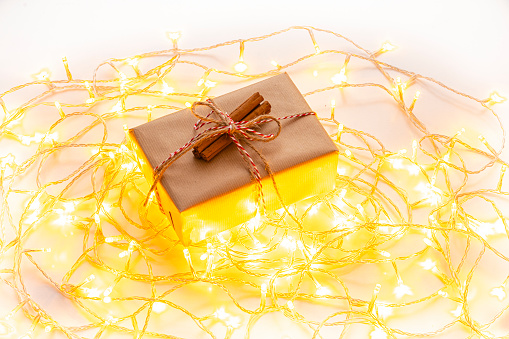 Christmas gift box wrapped with brown paper isolated on white background. String lights complete the composition