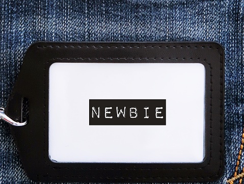 Black corporate ID card on jeans background with text label NEWBIE, refers to inexperienced newcomer wirker employee in the workplace,one who has just started doing activity or first jobber