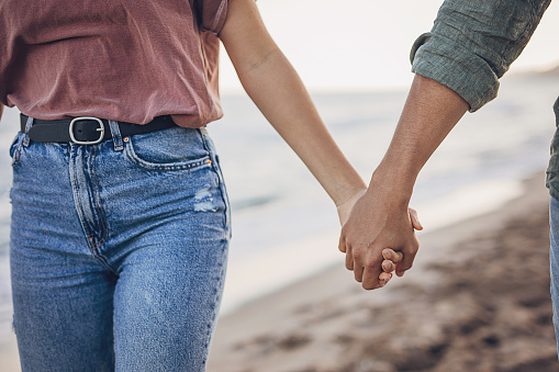 Man and woman, happy young couple holding hands on the beach by the sea.
