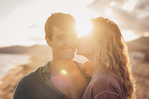 Man and woman, happy young couple standing on the beach by the sea. Woman is kissing a man.