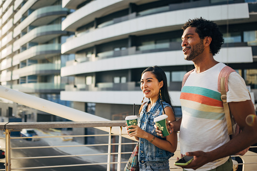 A smiling multiracial man enjoys the company of his smiling Asian friend as they walk around town and chat