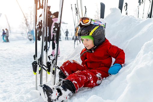 Cute adorable little kid boy enjoy having fun sledging down hill of snow heap snowdrift at alpine mountain skiing resort on bright winter day. Toddler beginner skier rest of training in ski school.