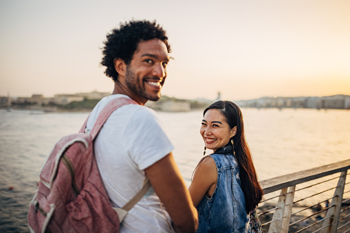 Portrait of a multiracial loving couple standing leaning against a fence overlooking the sea