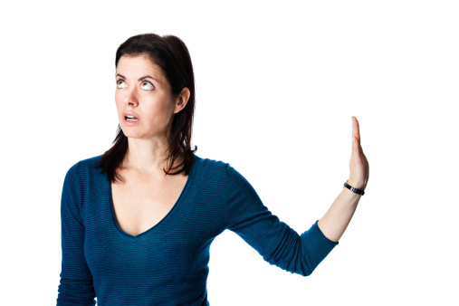 Fed up mature woman in a blue top gestures to talk to her hand to her right while looking up in exasperation.
