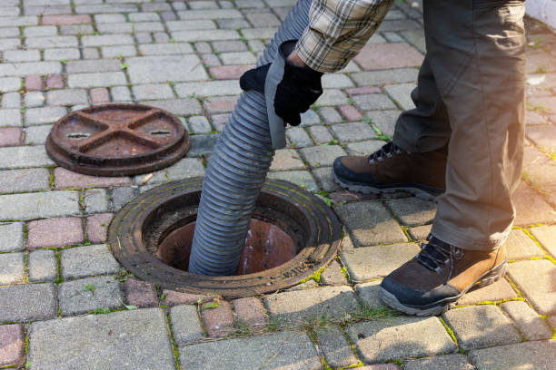 worker holding pipe and pumping out household septic tank. drain and sewage cleaning service stock photo