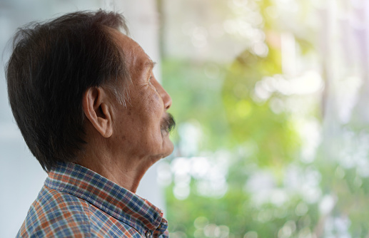 Side view portrait of Asian elderly man wearing striped shirt standing and look outside, copy space