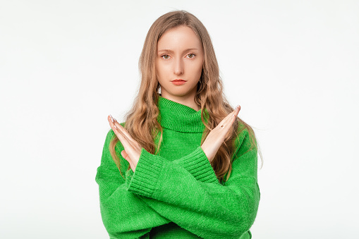 Serious woman making a rejection gesture, stopping you from something, frowns, preventing, rejecting something, standing over white studio backdrop