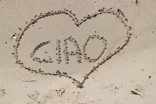 A scenic sandy shoreline with a heart-shaped 'Ciao' sign in the foreground