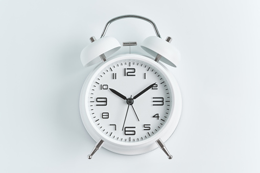 Close-up of a white alarm clock on a white background, ten o'clock.