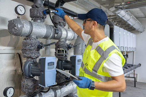 Technician Checking Heating System In The Boiler Room With Tablet In Hand