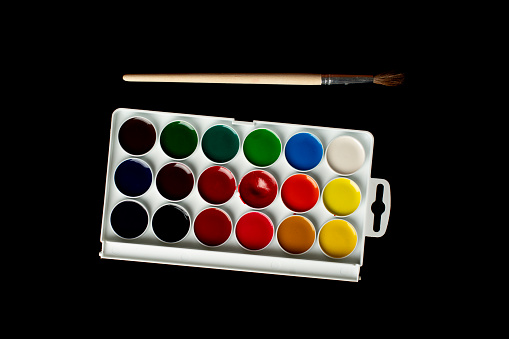 Set of watercolor paints and brushes for painting on a black background.