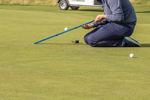 Groundsman using a stimpmeter on a golf course green allowing the ball to roll down the meter until it releases it at 22 degrees. The distance travelled provides a stimp value for the green.