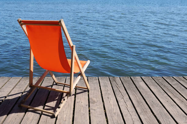 empty foldable beach chair on wooden deck overlooking calm water lake with copy space