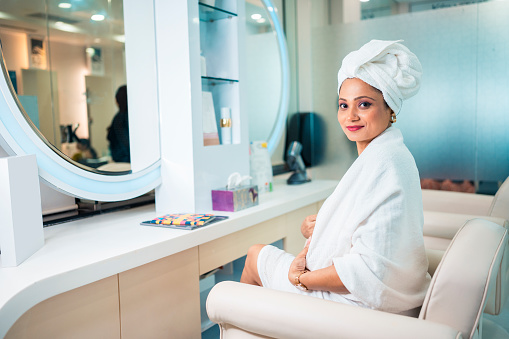 Relaxed young Caucasian woman wearing hair towel after beauty treatment or Hair Spa and sitting in Beauty salon, Looking at mirror in salon.