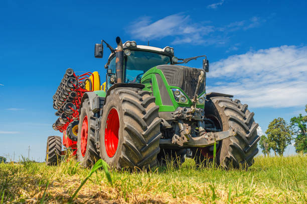 istock Bright tractor with field drill. Low angle view through grass to equipment. Blue sky background. 1678353391
