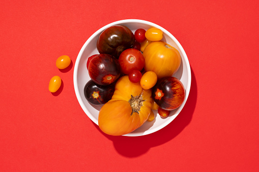 Colorful tomatoes in a white plate on yellow, green, red, yellow, white,  background, top view