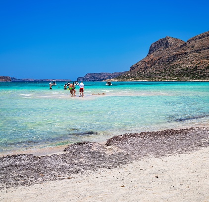 Crete, Greece - 22 june 2023: Bathers stroll through beautiful crystal clear waters beach with yellow sand at Balos lagoon on Crete, Greece