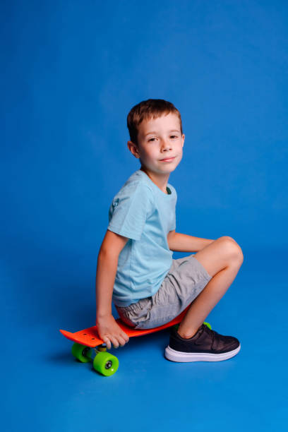 istock serious boy in blue mockup T-shirt sitting on skateboard over light blue studio background 1678421510