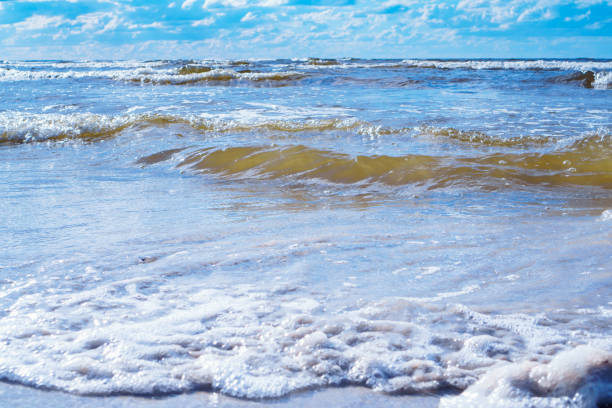 istock Bright blue sky with white clouds almost merges with sea waves with foam rolling on shore. Meditation and relaxation. 1678422639